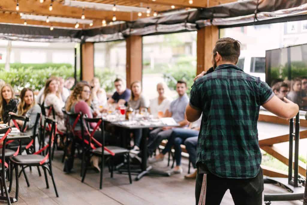 a man is speaking in front of a group of people inside a restaurant